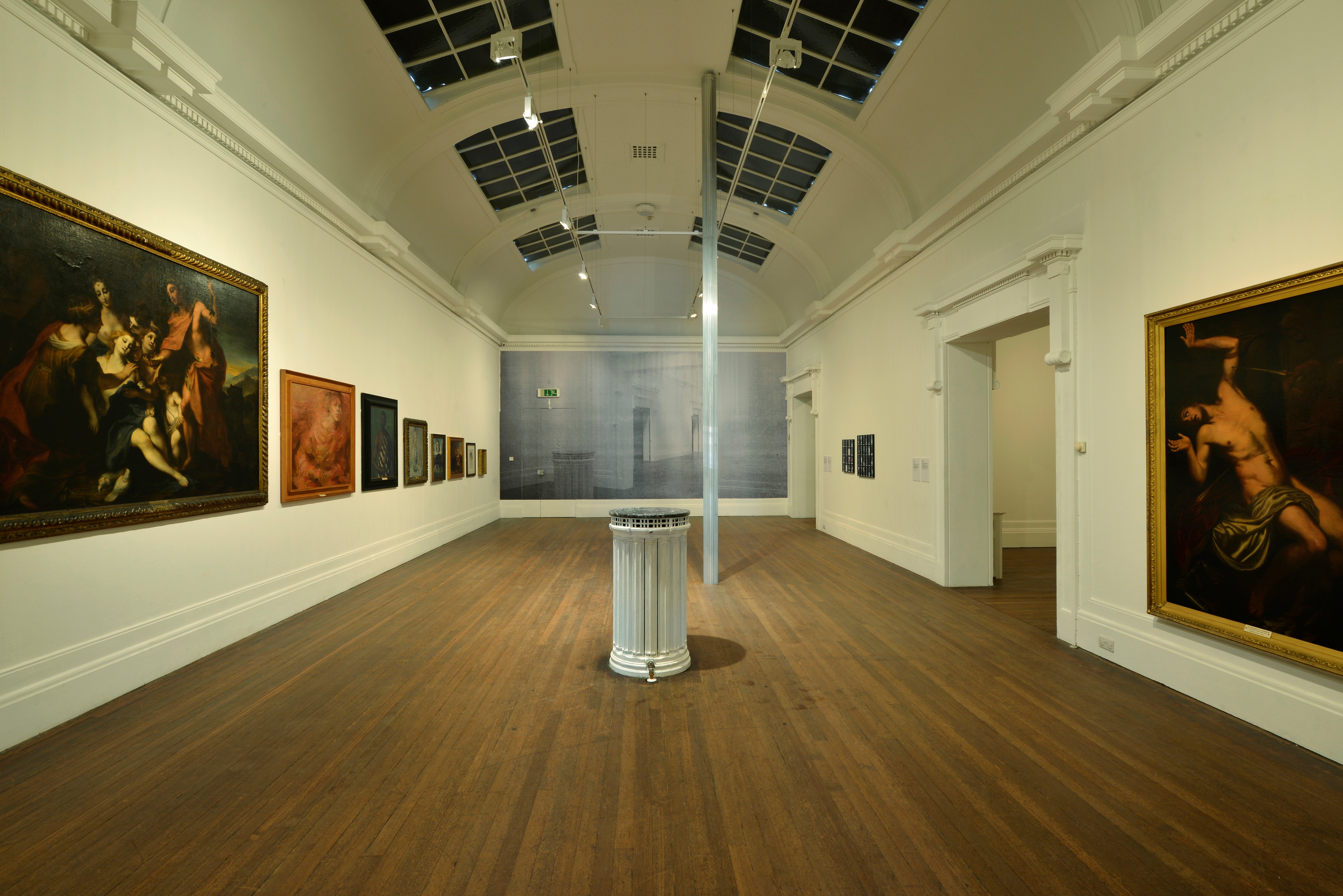 Various paintings from The Grundy Art Gallery’s permanent collection and commissioned artworks. The paintings are hung in size order from largest to smallest as viewed from entering gallery. The far wall of the gallery features a full wall vinyl photograph of galley, an aluminium pillar reaches from floor to ceiling two thirds of the way down the gallery. The artworks were included in the exhibition Haunted House.