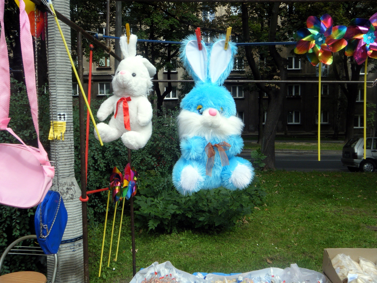 Objects hanging on washing line in park. Objects include two stuffed toy rabbits and foil hand windmills. Included in the Exhibition Leo Fitzmaurice and Paul Rooney: Blank Stir.