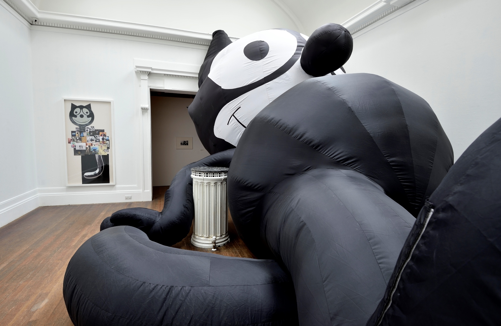 Large black and white inflatable Felix The Cat, and collage of various images of or relating to Felix The Cat. The inflatable Felix The Cat fills over half of the gallery space. Included in the exhibition Mark Leckey, This Colossal Kat, That Massive Mog.