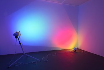 2 colour tinted floor based lights that create a red to blue colourfield upon gallery wall. The artwork was included in the exhibition Sensory Systems.