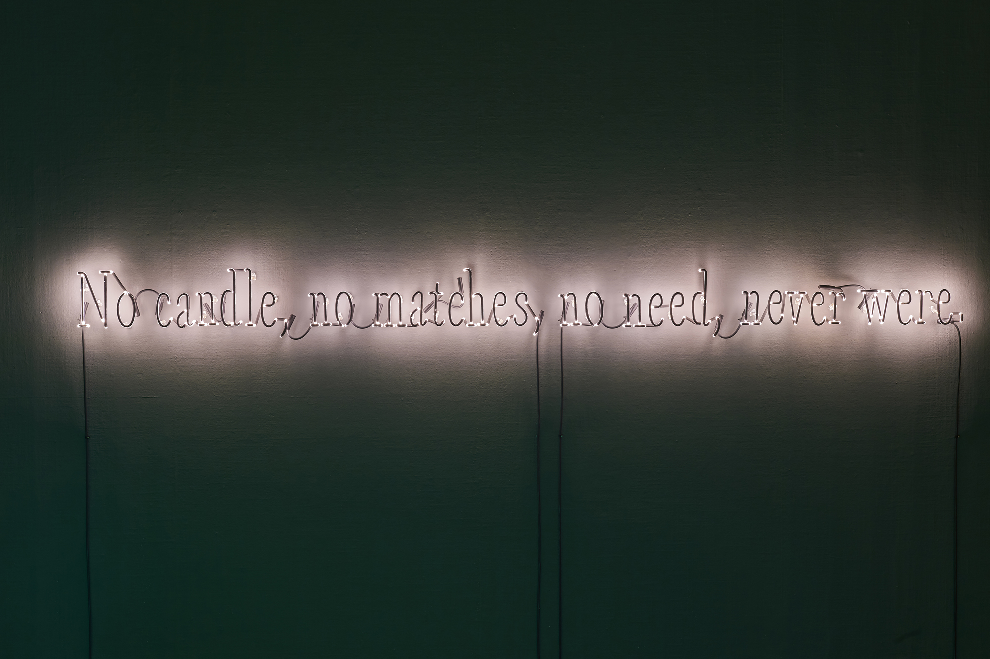 Neon artwork. The artwork consists of the words No candle no matches no need never were. The neon work is in white, the letters are backlit by masking the light from the front. Artwork was included in the exhibition Paper, Canvas, Neon.